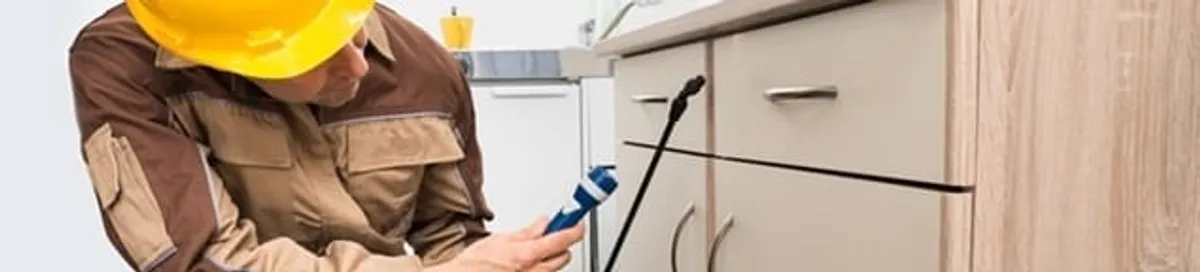 Roach exterminator applying treatment under kitchen cabinets in Minneapolis, MN