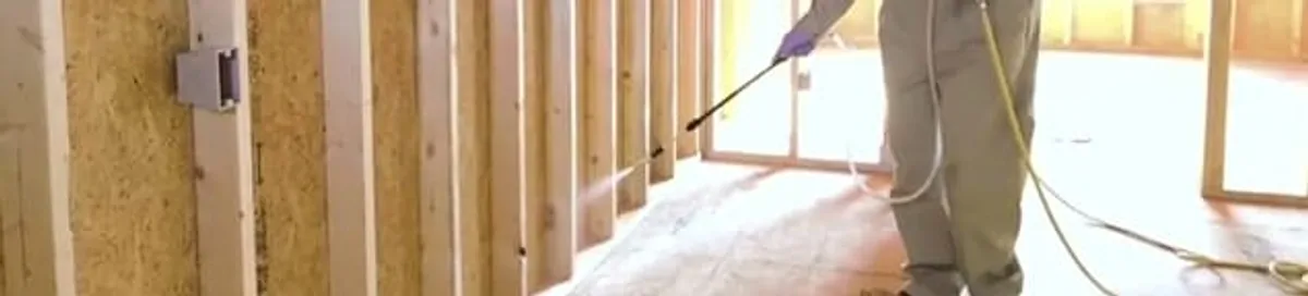 Termite treatment technician applying spray along framing and unfinished walls in Minneapolis, MN